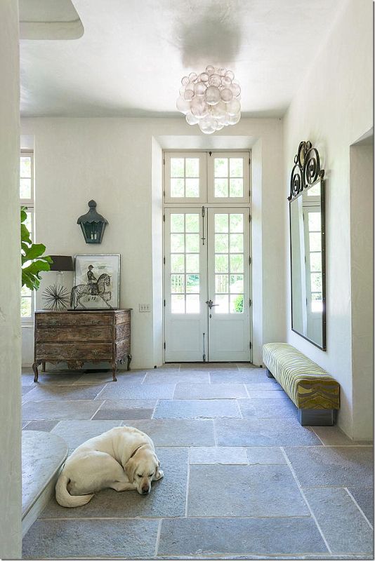 An internal photo of an entrance to a house which uses raw stone tiles. A dog lies sleeping to the left in the foreground.