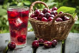 A cup of cherry juice placed next to a basket full of fresh cherries
