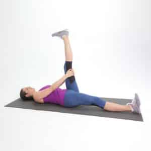 Woman lying on her back and stretching her left leg by pulling it upwards towards her chest