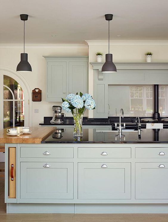 A kitchen displaying blue cabinets, hanging black lamps and dark counter tops