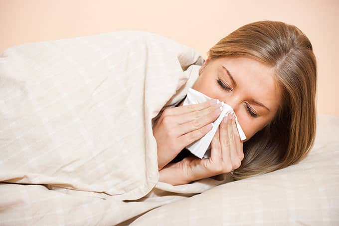 A woman lying in bed on her side, blowing her nose with a tissue