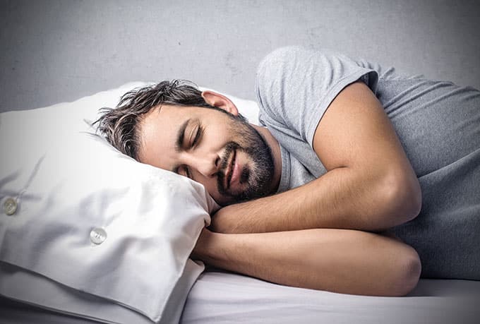 A bearded man sleeping on his side and facing the viewer