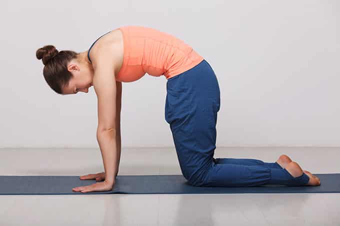 A woman leaning on the ground, her palms and lower legs supporting her, as she arches her back outwards