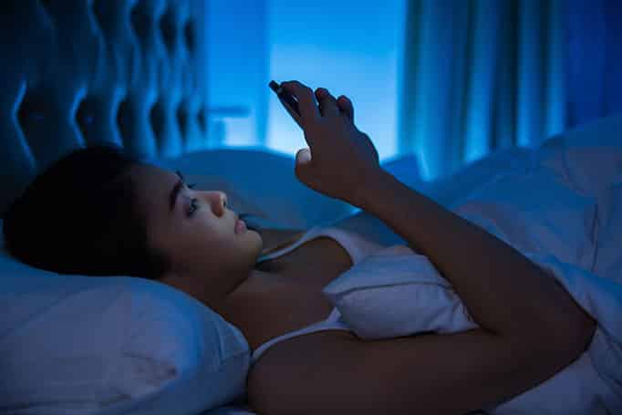 A woman lying on her back in bed using a mobile phone in a dark room