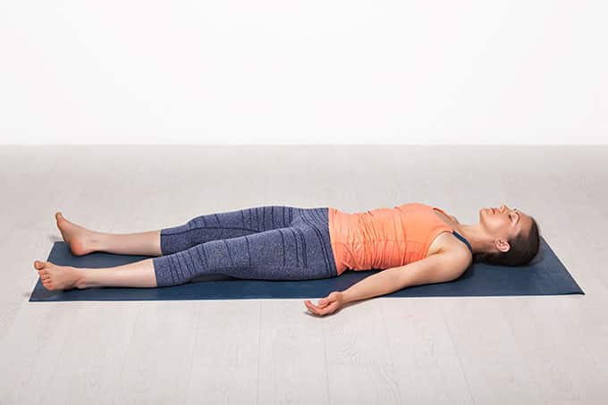 A woman lying face up on a yoga mat with her arms placed comfortably to her sides