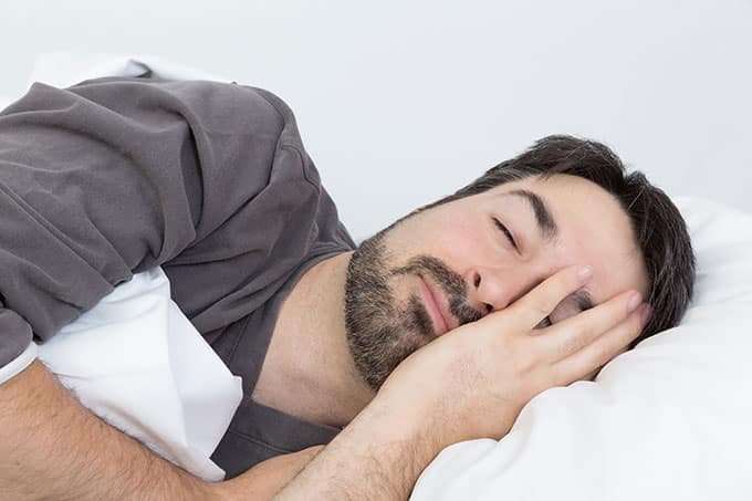 A bearded man sleeping on his side facing the viewer