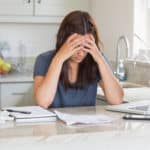 A woman holding her head in her hands as she ponders financial troubles