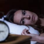 Woman lying awake in bed looking at an alarm clock in the foreground